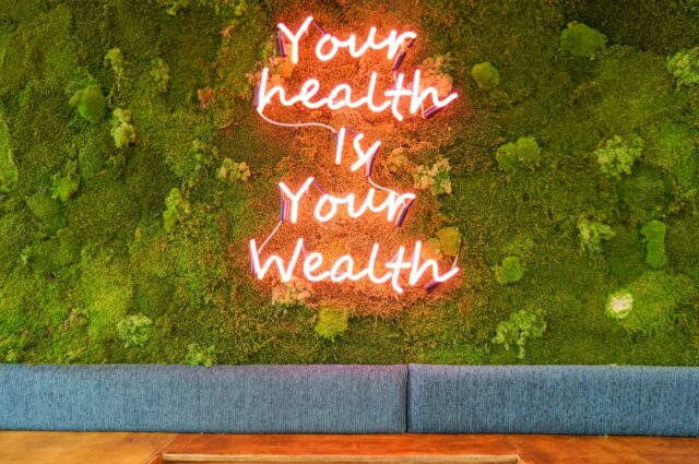 neon sign on moss wall saying 'your health is your wealth'